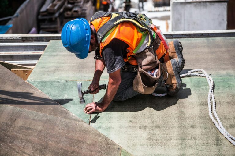 A commercial renovation with a  skilled construction worker in protective gear hammering a rooftop panel.