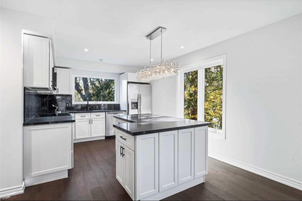 Modern white kitchen renovation in Toronto with island, black countertop, and updated lighting